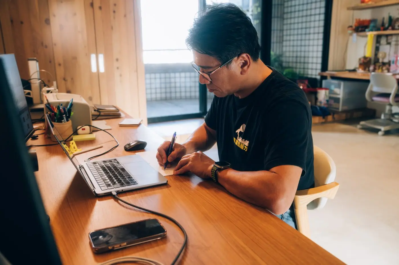 福哥在自家工作桌前，一邊看筆電一邊手寫當天的計畫